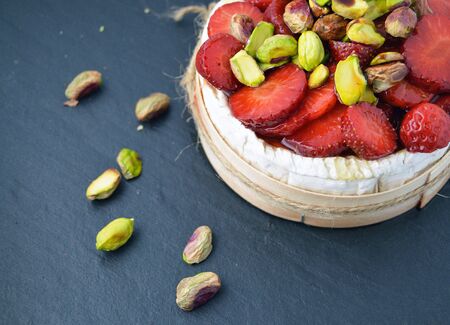 Baked camembert cheese with marinated strawberries and pistachios in wooden box on black slate backgroundの写真素材