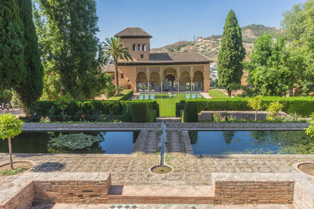 El Partal. A large central pond faces the arched portico behind which stands the Tower of the Ladies, inside the Alhambra of Granada, Andalusia, Spain, Europe on a bright sunny day with clear blue skyの写真素材