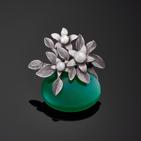 Silver brooch with big green glossy stone and pearls on black backgroundの写真素材