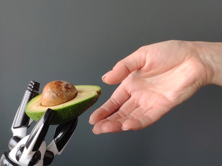 A robot's hand stretches an avocado into a young woman's hand, background or concept, free space for text.の写真素材