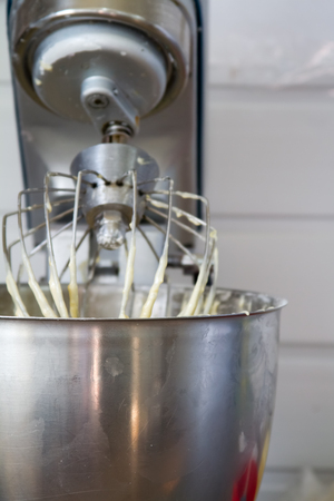 Closeup of electric mixer with whipped smooth dough for cake. Batter being whipped. Mixing white dough in bowl with motor mixer, baking cakeの写真素材