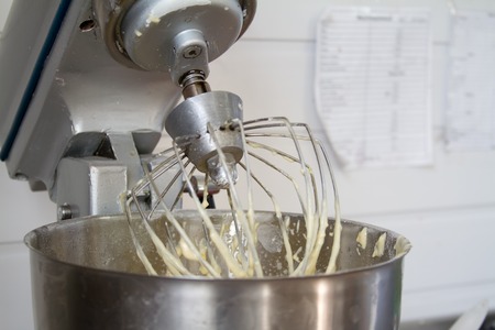 Closeup of electric mixer with whipped smooth dough for cake. Batter being whipped. Mixing white dough in bowl with motor mixer, baking cakeの写真素材