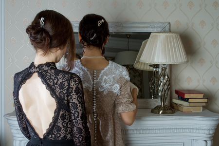 Two young women in vintage dresses look at each other through a mirror, a reflection of love. Added a small grain, imitation of film photography.の写真素材