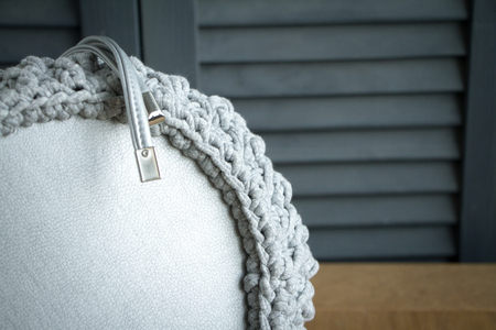 Extreme close-up of a handmade knitted bag in detail. Gray bag with leather bottom and straps. Selective soft focus.の写真素材