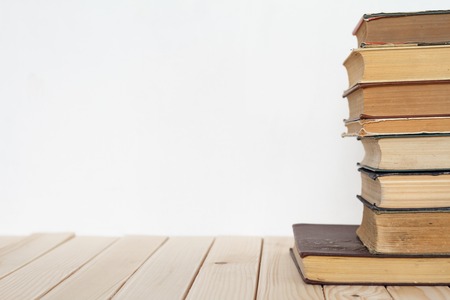 A stack of vintage books for business and education on a wooden surface against a white wall, back to school concept.の写真素材
