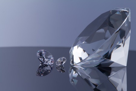 Huge diamond and several chic crystals on a black mirror surface and white background, shimmer and sparkle, free space for text.の写真素材