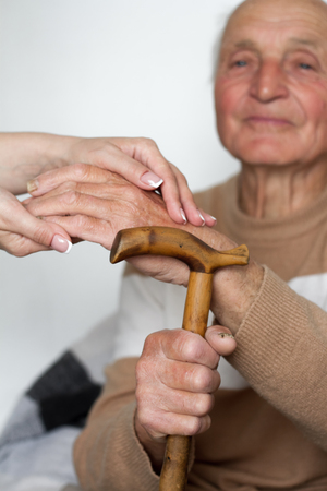Closeup of smiling senior mans hands and young girl caregiver holding hands on walking stick, concept of care for young people about the elderlyの写真素材