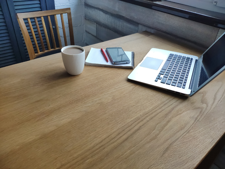 Male hands holding a mobile phone on the background of an open laptop and notebook, free space for...