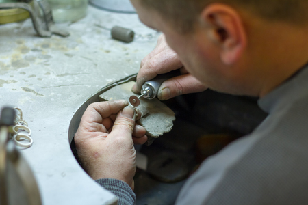 KHARKIV, UKRAINE - January 31, 2019: The master jeweler holds the working tool in his hands and makes jewelery at his workplace in the jewelry workshop.のeditorial素材
