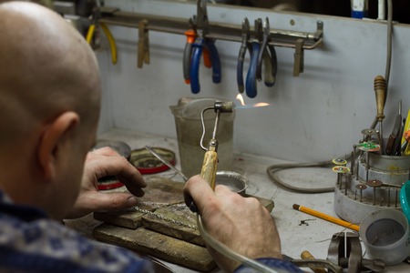 KHARKIV, UKRAINE - January 31, 2019: The master jeweler holds the working tool in his hands and makes jewelery at his workplace in the jewelry workshop.のeditorial素材