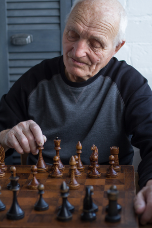 An old man is sitting in front of a chessboard, thinking and making the first move in the game, copyspaceの写真素材