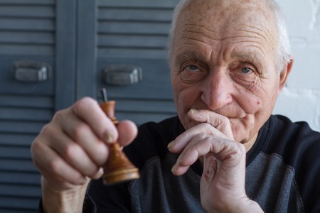 The old man holds in his hands the chess piece of the king, the concept of winning or losing, copyspaceの写真素材
