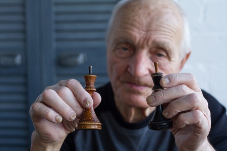 The old man holds in his hands the chess piece of the king, the concept of winning or losing,...