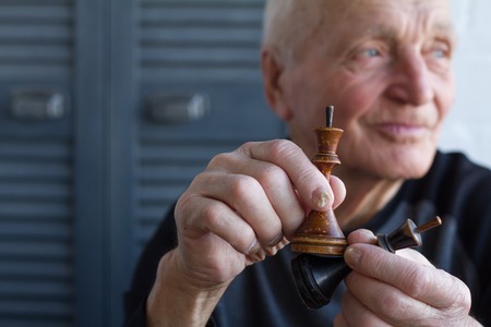 The old man holds in his hands the chess piece of the king, the concept of winning or losing, copyspaceの写真素材