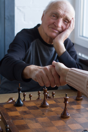 An old man shakes hands with an opponent in a game of chess, he lost and acknowledges it, copyspace.の写真素材