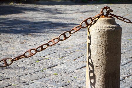 Closeup of a stone fence pillar and chain on a stone pavement background, copyspaceの写真素材