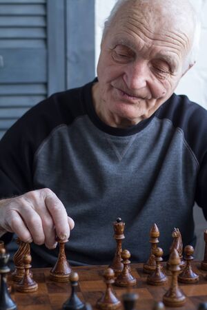 An old man is sitting in front of a chessboard, thinking about the next move in a chess game, copyspaceの写真素材