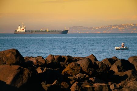 Unrecognizable man sailing on a boat with oars in the sea, a fisherman in a boat on the background of a huge liner, copyspaceの写真素材