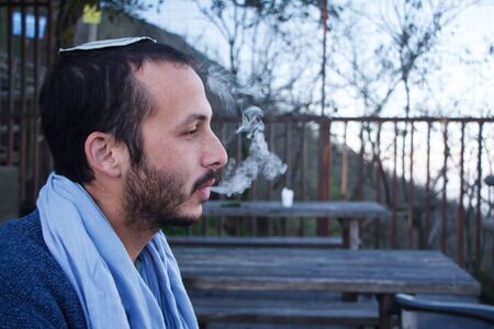 Naples, Italy - November 09, 2018: Profile of a young Jewish man in a traditional Jewish Kippa headdress talking, smiling, smoking on top of Mount Vesuvius in Naples, Italyのeditorial素材