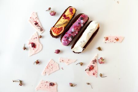 A set of three eclairs with different fillings and a design isolate on a white surface decorated...