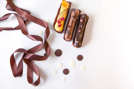 A set of three eclairs with different fillings and design isolate on a  surface decorated with chocolate drops and brown silk ribbon,の写真素材