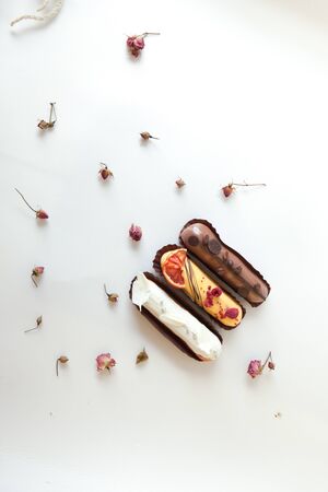Set of three eclairs with different fillings and design. Isolate on a white surface decorated with dry roses, copyspaceの写真素材