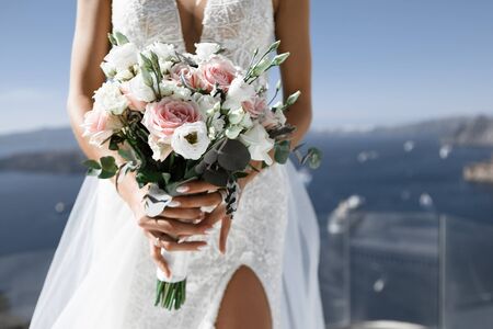 Bride in a white dress with a slit holds bouquet on background of sea and sky, soft focusの写真素材