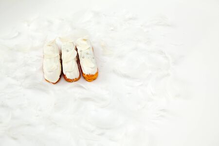 A set of three eclairs with white chocolate decor isolate on a white surface decorated with white feathers, copyspaceの写真素材