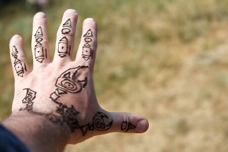 An arabic mehendi scorpion drawing on a mans hand on a blurred background of meadows, selective focusの写真素材