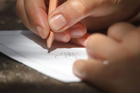 Closeup childs hand draws a flower with a pencil on a white sheet of paper, selective focus