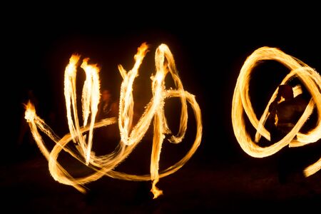 An artist shows a fire show at night spinning torches, circles of fire and loops