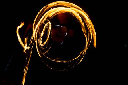 An artist shows a fire show at night spinning torches, circles of fire and loops