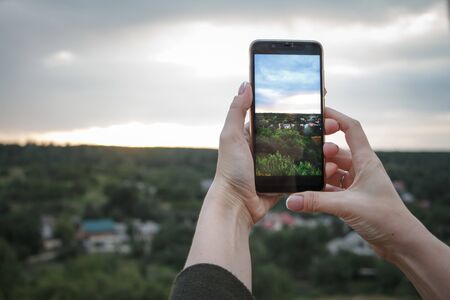 Closeup of female hands shoot a beautiful landscape with green hills and sunset on a smartphone, selective focusの写真素材