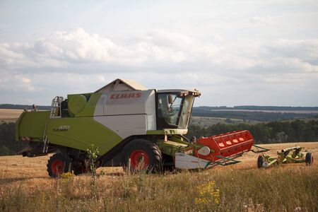 Kharkiv, Ukraine - July 16, 2019: Combine harvester with a raised mechanism rides the stubble after harvesting wheat fields for harvestingのeditorial素材