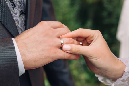Closeup of the hand of the bride puts a wedding ring on the grooms finger, the ceremony on the street, selective focusの写真素材
