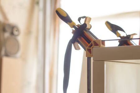 Gluing and fixing wooden furniture with a few clamps on a blurred background of carpentry workshop,...
