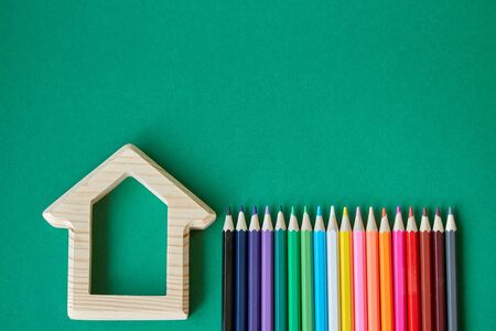 A wooden house figurine and several colored pencils isolate on green background, concept back to school, selective focusの写真素材