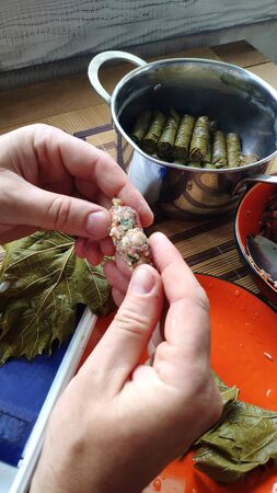 Closeup of male hands making Dolma, tolma, sarma, dolmah stuffed grape leaves with rice and meat...
