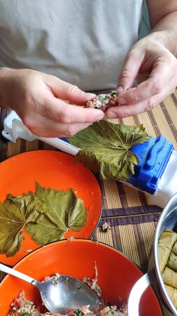 Closeup of male hands making Dolma, tolma, sarma, dolmah stuffed grape leaves with rice and meat using a special device, traditional Caucasian, Ottoman, Turkish and Greek cuisine, selective focusの写真素材