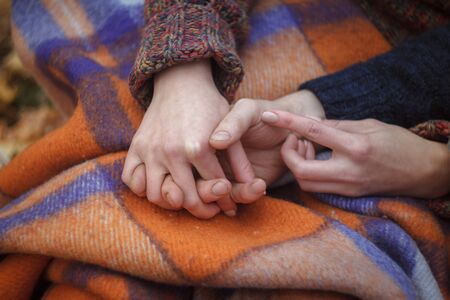 Close up of male and female hands entwined against the background of a warm woolen plaid, a cozy autumn concept, selective focusの写真素材