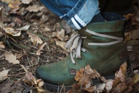 Close up of a leg in green hiking boots with laces in the autumn forest against a background of yellow fallen foliage, selective focusの写真素材