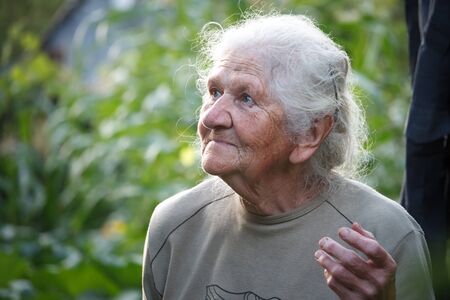 Closeup portrait of an old woman with gray hair smiling and looking up, face in deep wrinkles, selective focusの写真素材