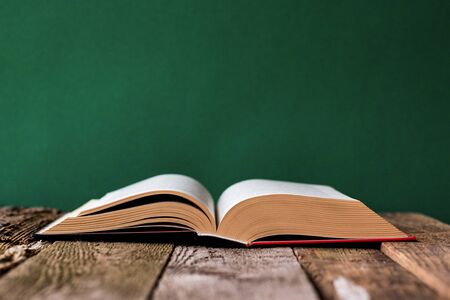 Back to school concept, open book on old wooden surface against a backdrop of clean green chalk board, selective focus, copyspaceの写真素材