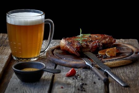 Still life with big fried steak, a glass of beer, mustard and cutlery on an old wooden tabletop, the concept of Oktoberfest and St. Patrick's Dayの写真素材