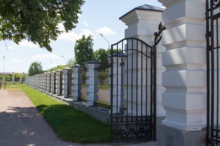 A fence with columns and a lattice near the asphalt road and english park, copy spaceの写真素材
