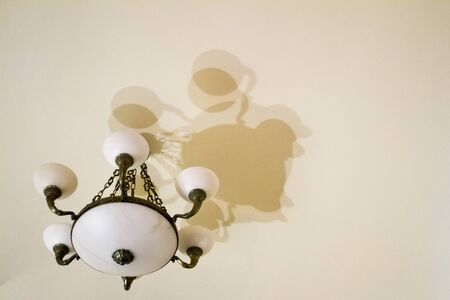 Bottom view of a metal bronze chandelier with white shades against a white ceiling with many shadows, copy spaceの写真素材