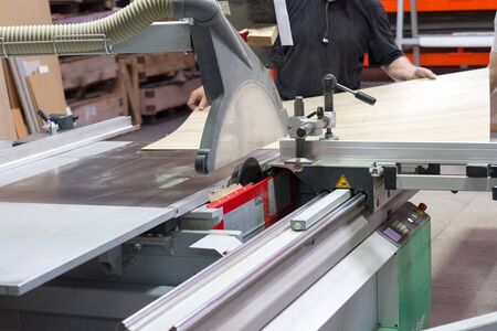 Close up of a furniture workshop worker sawing a workpiece with a circular saw on a machine,...