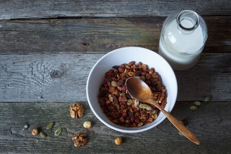 Crunchy honey granola bowl with flax seeds, cranberries and bottle of milk on a table, healthy and fiber food, selective focusの写真素材