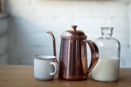 Close up coffee cup, copper coffee pot and a bottle with milk on a light wooden surface, selective focusの写真素材