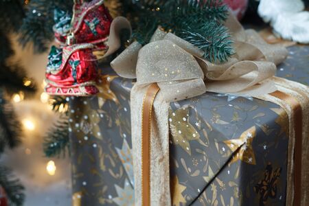 Close up of a beautifully wrapped and tied up with a gold lace ribbon gift under the Christmas tree,...